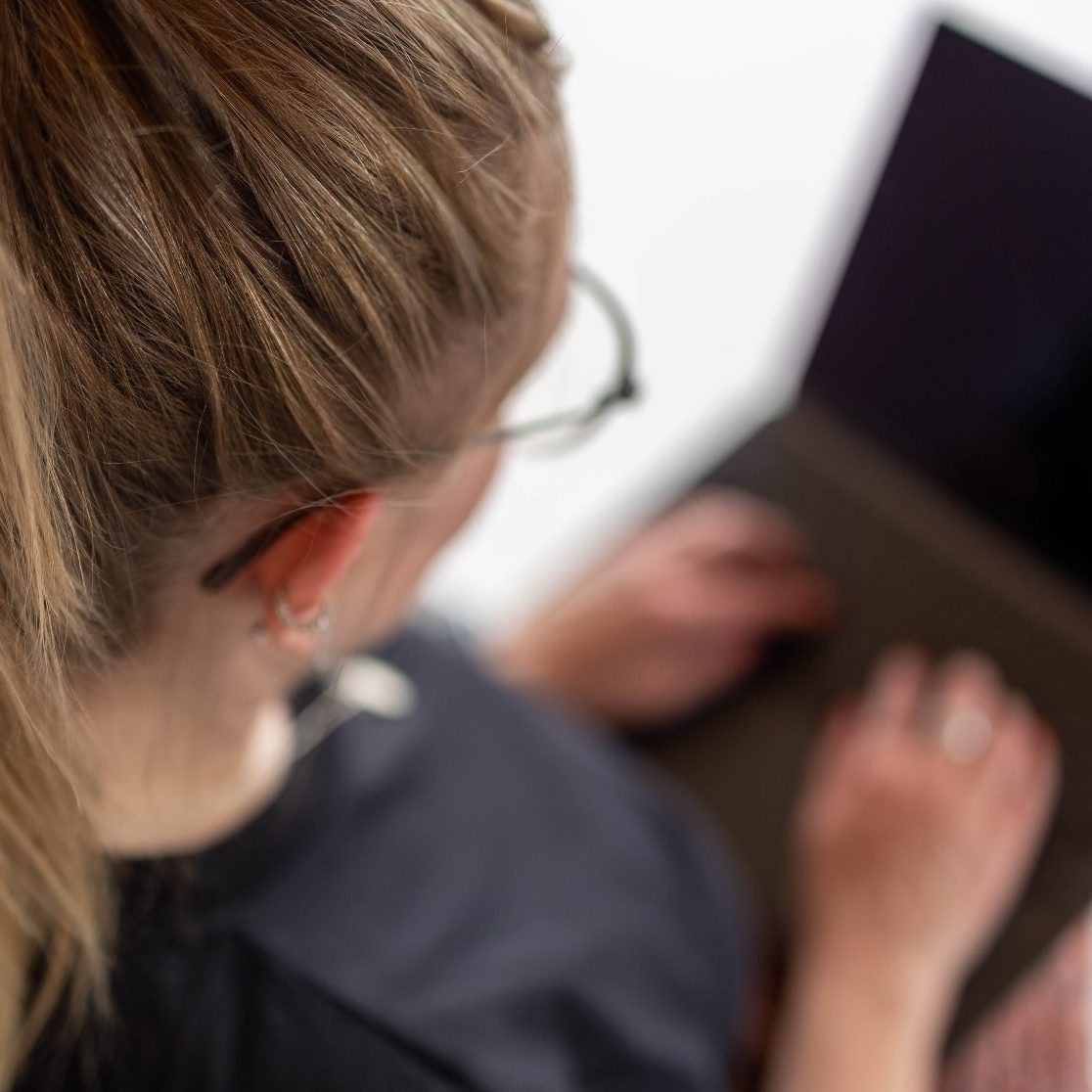 Eine Person arbeitet auf einem Laptop mit langem, blondem Haar und Brille.
